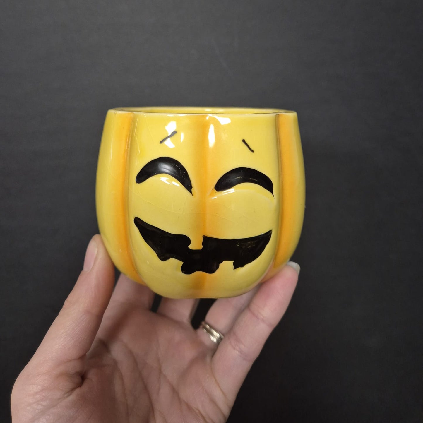 Hand holding a yellow cup with a black face design against a dark background